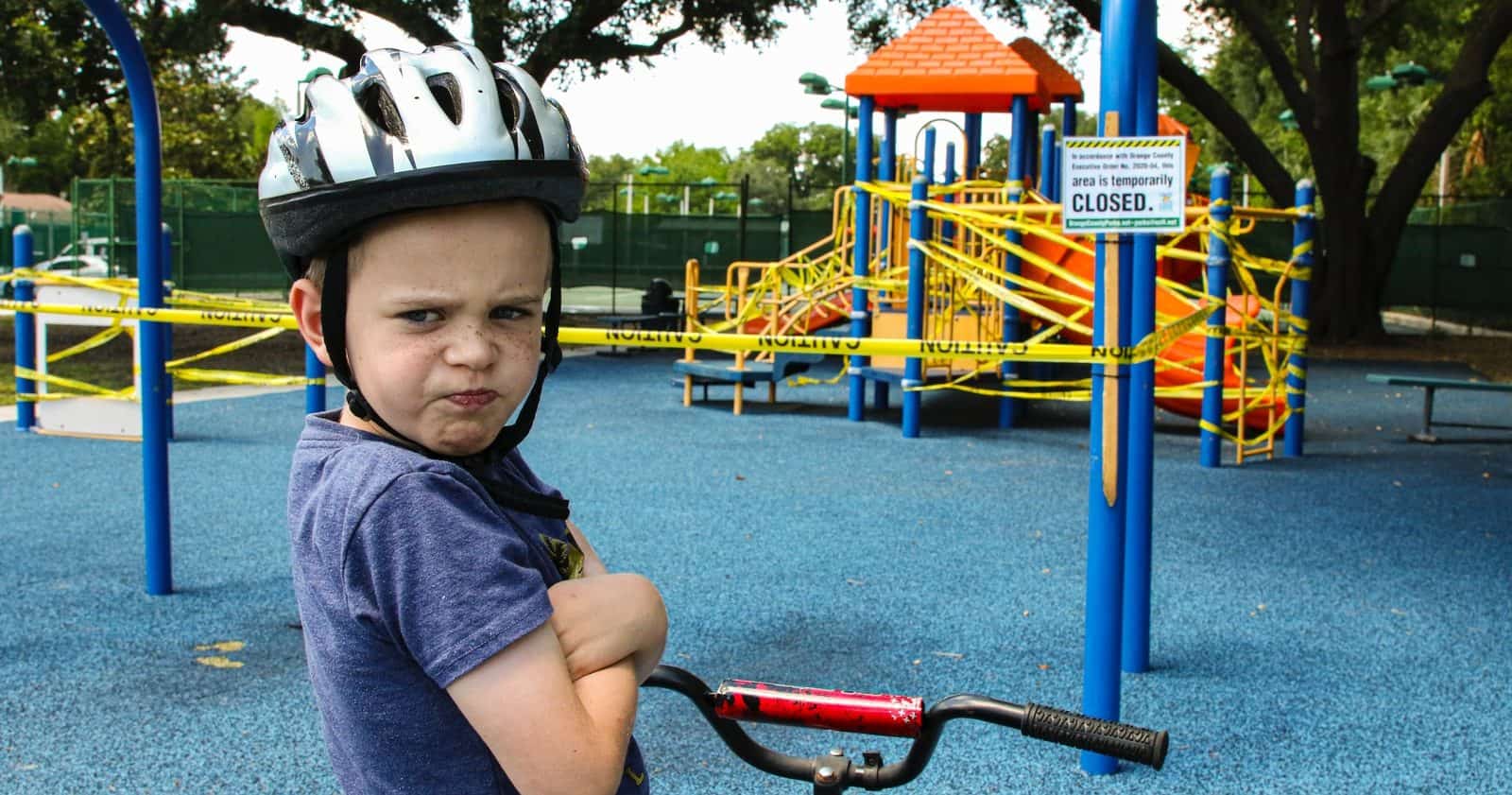 boy in blue denim vest and helmet riding red bicycle